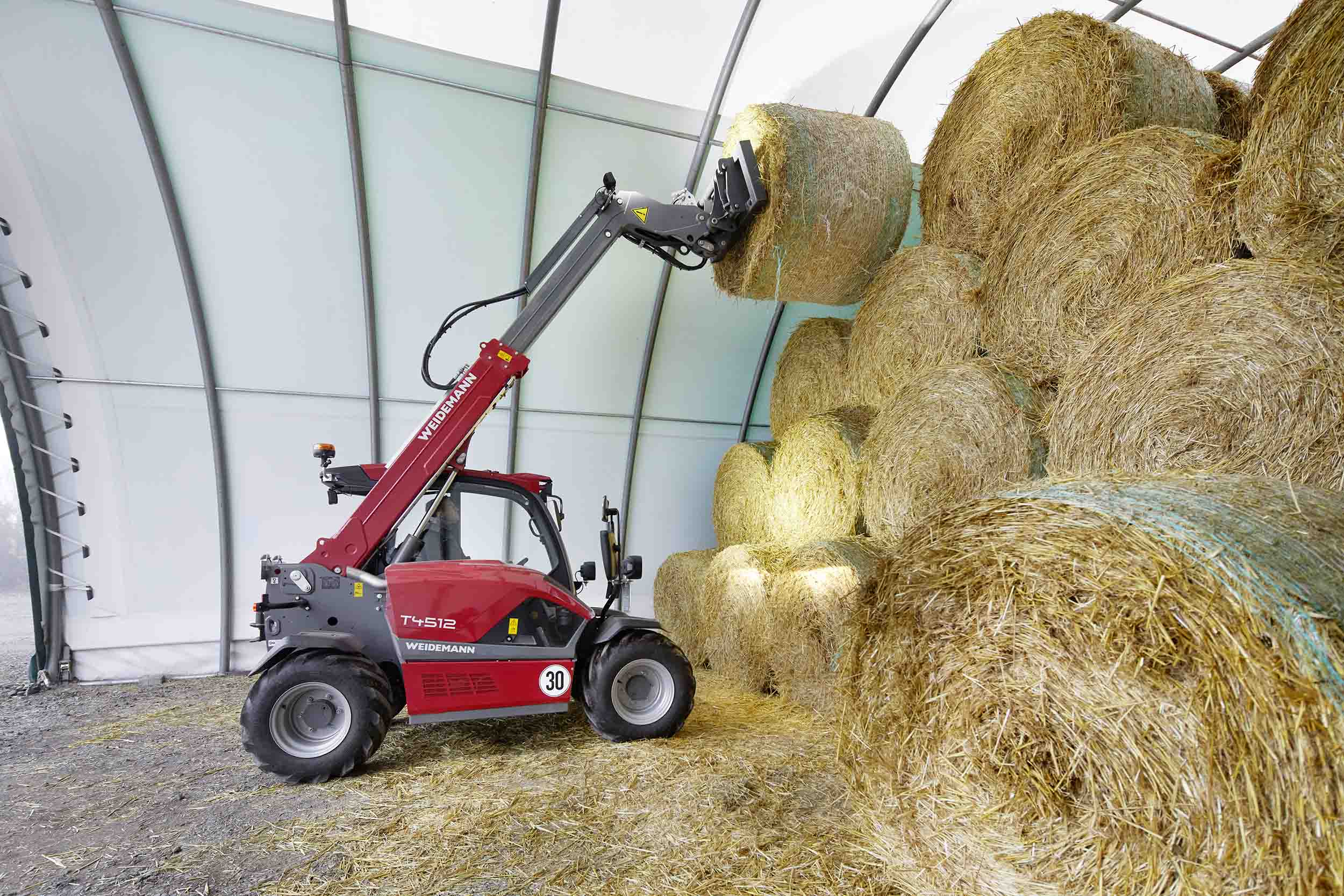 Weidemann teleskoplaster som stabler høyballer innendørs.